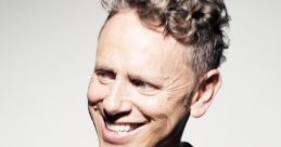 Martin L. Gore smiling, showcasing his iconic curly hairstyle, dressed in a stylish black shirt against a neutral background.