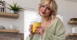 Kallmekris, wearing a cozy green cardigan and jeans, enjoys a yellow mug in a modern kitchen setting.