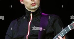 Matthew Bellamy performing live with a guitar, showcasing his iconic red hairstyle and energetic stage presence.