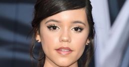 Jenna Ortega at a red carpet event, showcasing her elegant style with a shiny black off-shoulder dress and delicate jewelry.