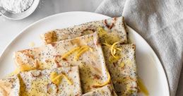 Delicious lemon-scented poppy seed crepes drizzled with olive oil, served on a white plate with a rustic napkin.