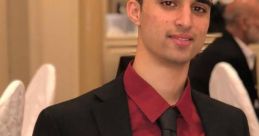 Young man in a black suit with a red shirt and tie, seated at an elegant event, showcasing a confident demeanor.