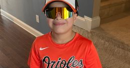 Young baseball player in Orioles gear smiling confidently, ready for practice or a game in vibrant orange and white uniform.