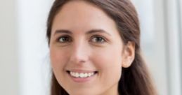 Smiling British woman with long brown hair, wearing a polka dot blouse in a bright, modern setting.