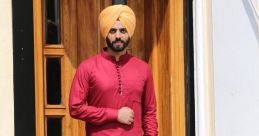 Man in a red kurta and yellow turban standing by a wooden door, showcasing traditional Punjabi attire and style.