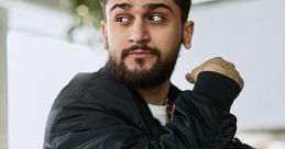 Stylish young man with a beard wearing a black bomber jacket, sitting at a modern cafe table, looking thoughtfully.