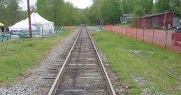 View down a rustic railway track surrounded by greenery and a tent, showcasing the charm of rural train routes.