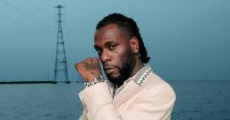 Burna Boy posing confidently on a boat, dressed in a stylish suit against a serene ocean backdrop.