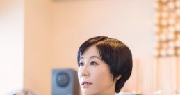 Yoko Kanno poised in a stylish gray outfit, reflecting her artistic elegance in a modern studio environment.