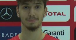 Berkcan smiles during a press conference, wearing a red sports jersey with Turkish flag, promoting basketball in Turkey.