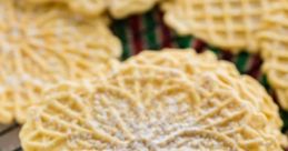 Golden pizzelles dusted with powdered sugar on a festive striped cloth, perfect for holiday celebrations.