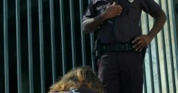 Police officer stands over a handcuffed individual seated on the ground, highlighting a serious arrest scenario.