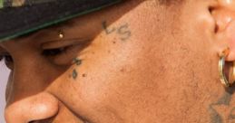 Profile of a man with unique tattoos and a camo cap, showcasing his distinctive style and personality.