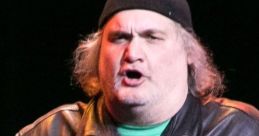 Artie Lange performs stand-up comedy on stage, wearing a black beanie and leather jacket, engaging the audience with humor.