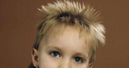 Child with a stylish spiky hairstyle, wearing a light blue polo shirt, looks directly at the camera with curious eyes.