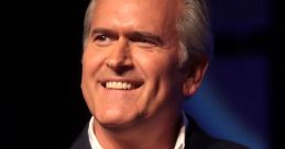 Bruce Campbell smiles while speaking into a microphone at a live event, showcasing his charismatic presence.