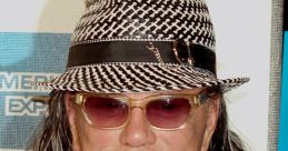 Mickey Rourke at a premiere event, wearing a stylish fedora and sunglasses, showcasing his unique fashion sense.