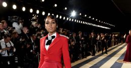 Janelle Monáe stuns in a bold red suit with dramatic cape, walking the Vanity Fair Oscars red carpet.