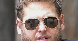 Jonah Hill wearing sunglasses and a black V-neck shirt, captured candidly outdoors, showcasing his unique style.