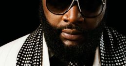 Rick Ross exudes style in a sharp polka dot suit with sunglasses and a red rose, showcasing his iconic fashion sense.