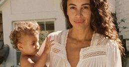 Mom holding a baby in a casual white dress, exuding warmth and tenderness in a serene outdoor setting.