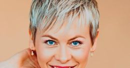 Smiling woman with short, blonde hair wearing an orange top, showcasing vibrant blue eyes against a warm background.