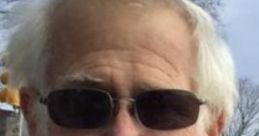 Smiling elderly man with white beard and sunglasses, reminiscent of online personality Angry Grandpa, outdoors in a park.