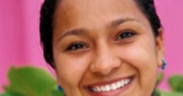 Smiling woman wearing traditional embroidered blouse and colorful jewelry, surrounded by lush greenery and pink background.