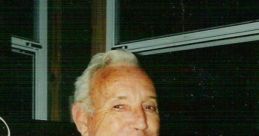 Smiling elderly man wearing a plaid shirt, seated indoors, exuding warmth and friendliness in a cozy setting.