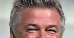 Alec Baldwin smiles brightly at a speaking event, showcasing his charismatic personality and signature hairstyle.