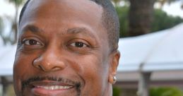 Chris Tucker smiles at an event, sporting a stylish black and gold patterned suit, showcasing his charismatic personality.