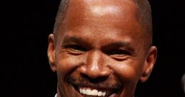 Jamie Foxx smiling at a panel event, wearing a denim shirt, with a water bottle visible in the foreground.