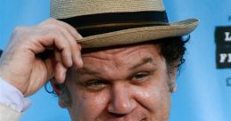 John C. Reilly tipping his hat, dressed in a light suit, smiling against a blue background at a film event.