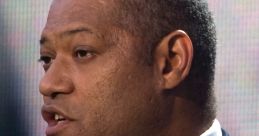 Laurence Fishburne speaking at an event, wearing a navy suit and pink tie, showcasing his leadership and charisma.