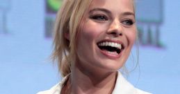 Margot Robbie smiles brightly while wearing a stylish white outfit at a promotional event, showcasing her radiant charm.