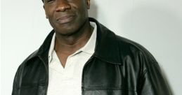 Michael Clarke Duncan smiles confidently in a black leather jacket and cap, showcasing his iconic style and charm.