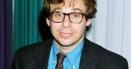 Rick Moranis smiling in a stylish outfit, featuring a blazer, blue shirt, and patterned tie, highlights his iconic 90s look.