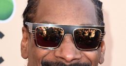 Snoop Dogg smiling confidently, wearing stylish sunglasses and a black jacket, exuding coolness at a red carpet event.