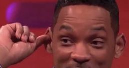 Will Smith playfully gestures during an interview, showcasing his stylish outfit and engaging personality.