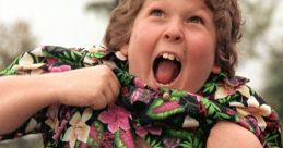 Chunk from The Goonies, laughing joyfully, wears a colorful floral shirt and plaid shorts in an energetic moment.