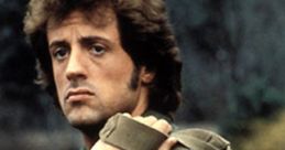 John J. Rambo with an intense expression, wearing military gear and carrying a heavy backpack in a rugged outdoor setting.