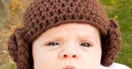 Cute baby dressed as Princess Leia in a cozy white outfit with a brown belt and iconic brown earmuff hat.