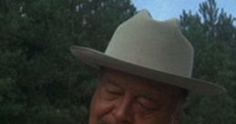 Sheriff Buford T. Justice in uniform, sporting a hat, with a reflective expression against a wooded backdrop.