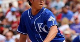 Pitcher in a blue Kansas City Royals uniform prepares to throw a pitch during a baseball game with cheering fans in the background.