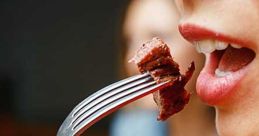 Close-up of a person about to eat a piece of meat on a fork, enjoying a delicious meal with friends.