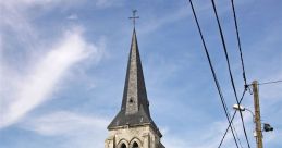 Historic church with a tall spire in a quaint French village, surrounded by greenery and a peaceful street scene.