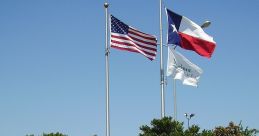 Flagpoles displaying the American and Texas flags at the entrance of Meadows Place, Texas, surrounded by lush greenery.