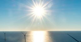 Sunrise over calm waters with offshore wind turbines harnessing renewable energy, reflecting sunlight across the sea.