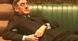 Jacob Rees-Mogg reclining on a green bench in Parliament, capturing a moment of relaxation during a session.