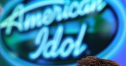 Simon Cowell at an American Idol event, showcasing his iconic serious expression and the show's logo in the background.